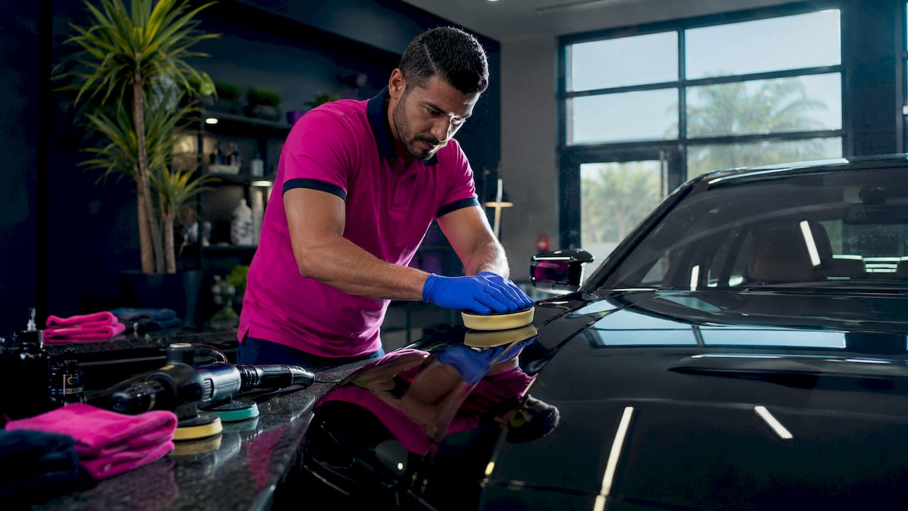Technician polishing luxury car hood in workshop