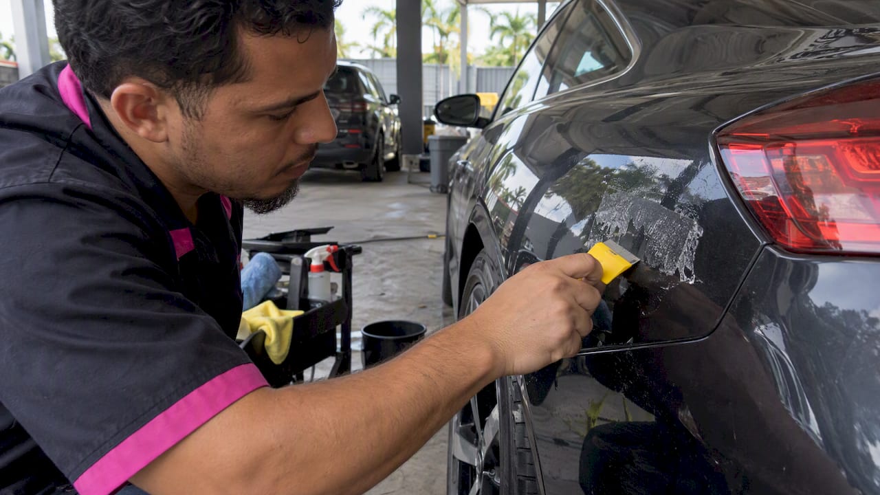 Technician lifting decal adhesive from luxury car paint